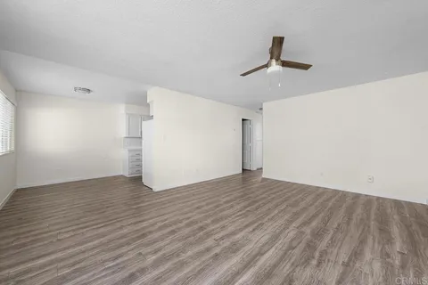 an empty room with wooden floor ceiling fan and windows