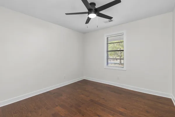 an empty room with wooden floor ceiling fan and windows
