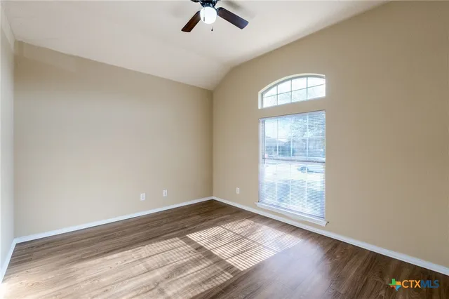 an empty room with wooden floor fan and windows