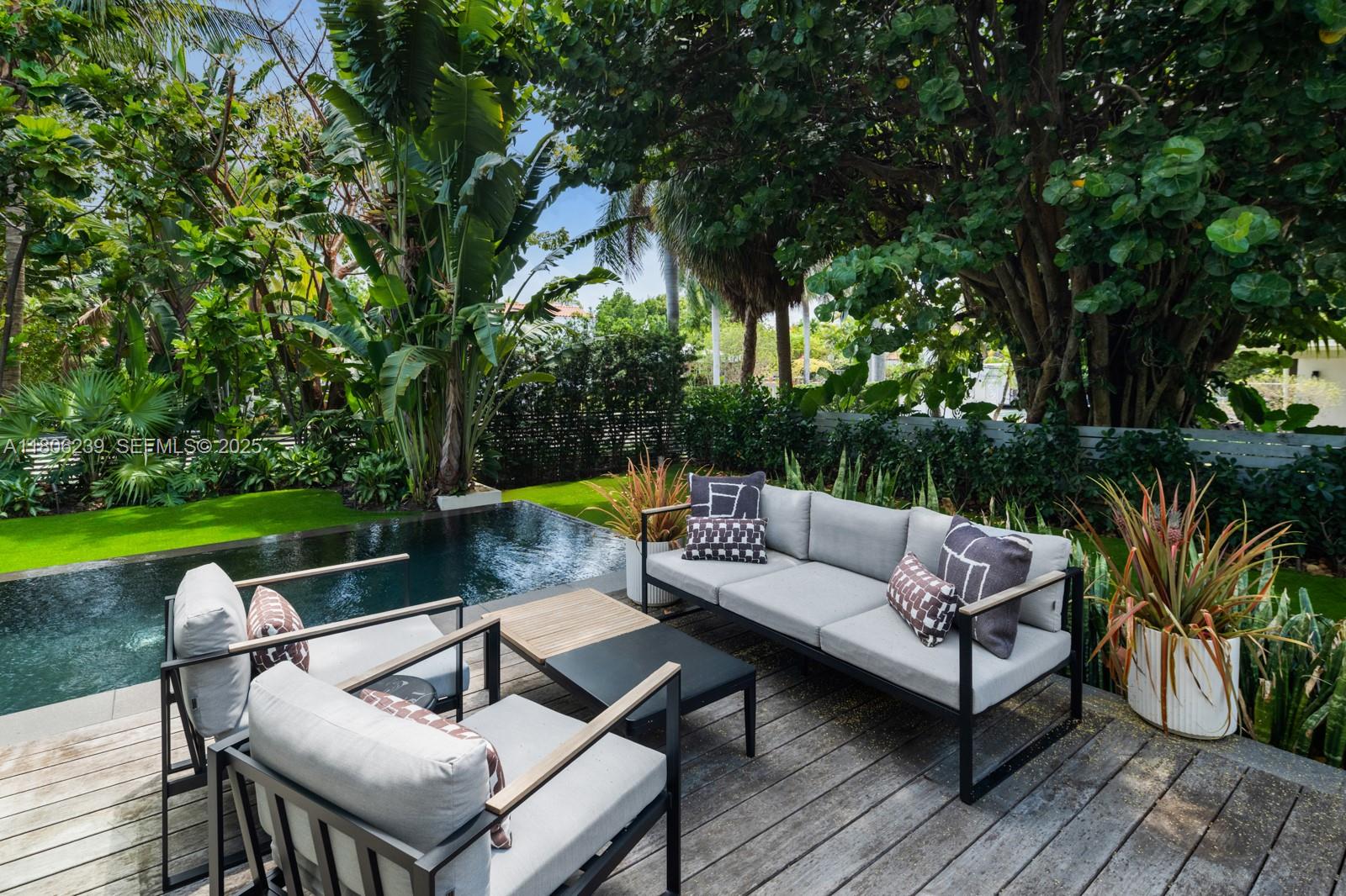 4700 Meridian Avenue Miami Beach, FL 33140 - Photo 27 of 64 a view of a patio with couches and a table and chairs with wooden fence and large trees