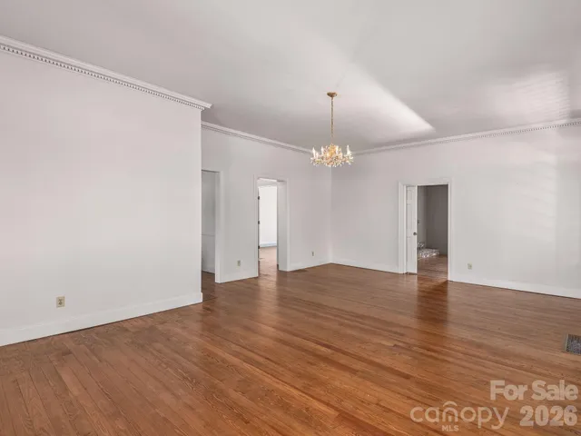 a view of an empty room with wooden floor and chandelier