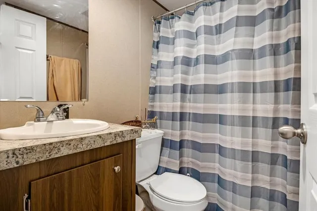 a bathroom with a granite countertop sink a toilet a mirror and shower curtain