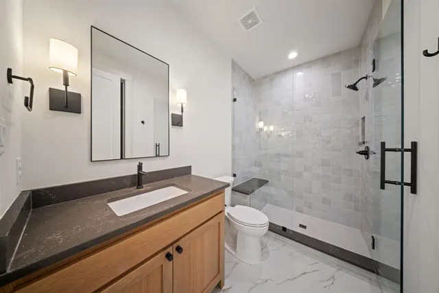 a bathroom with a granite countertop sink a toilet a mirror and shower