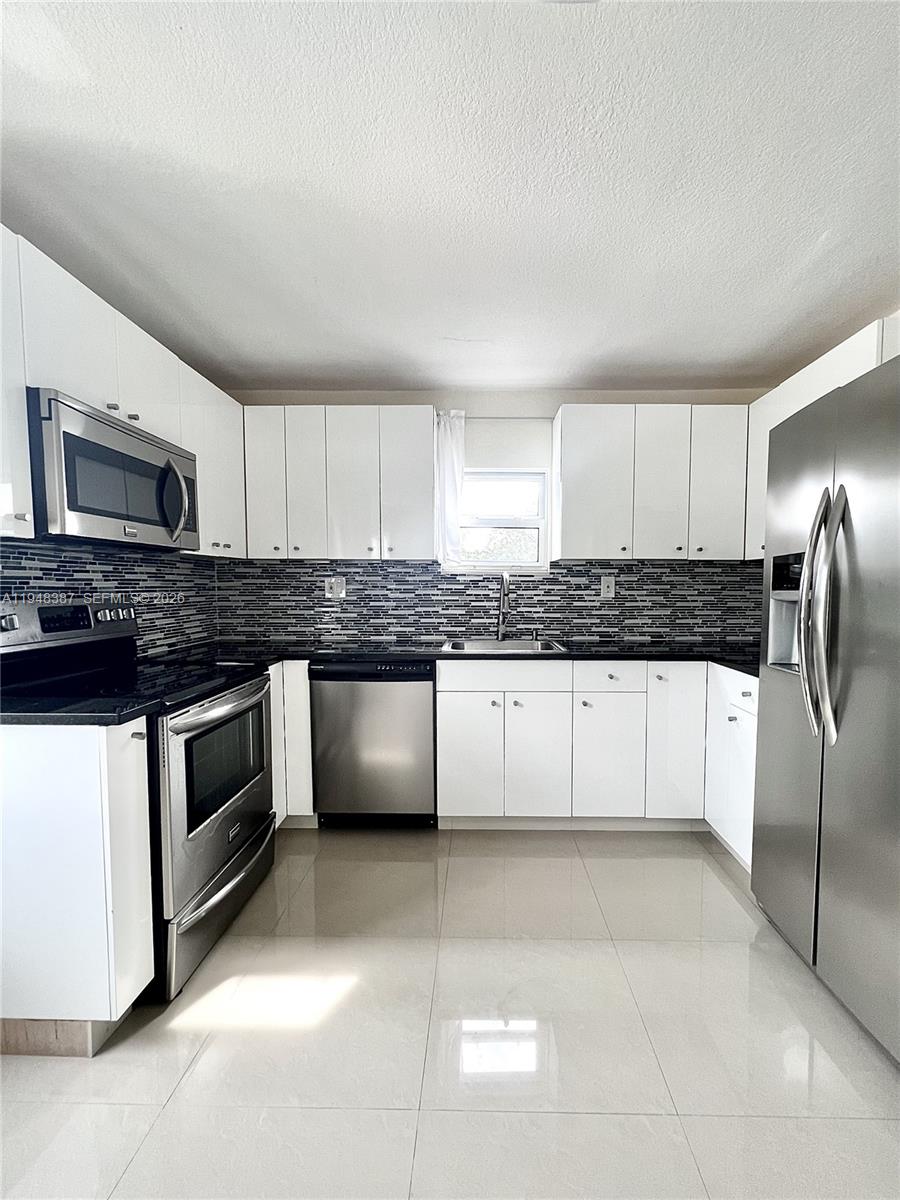 a kitchen with granite countertop a refrigerator and white cabinets