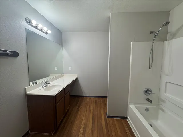 a bathroom with a tub sink vanity granite and shower