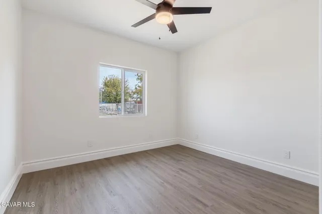 an empty room with wooden floor ceiling fan and windows