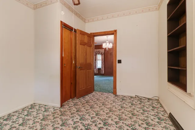 an empty room with chandelier fan and kitchen view