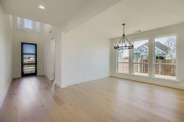 an empty room with wooden floor chandelier and windows