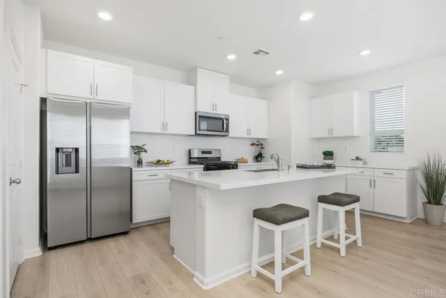 a kitchen with stainless steel appliances granite countertop a microwave a stove a sink a refrigerator and white cabinets with wooden floor