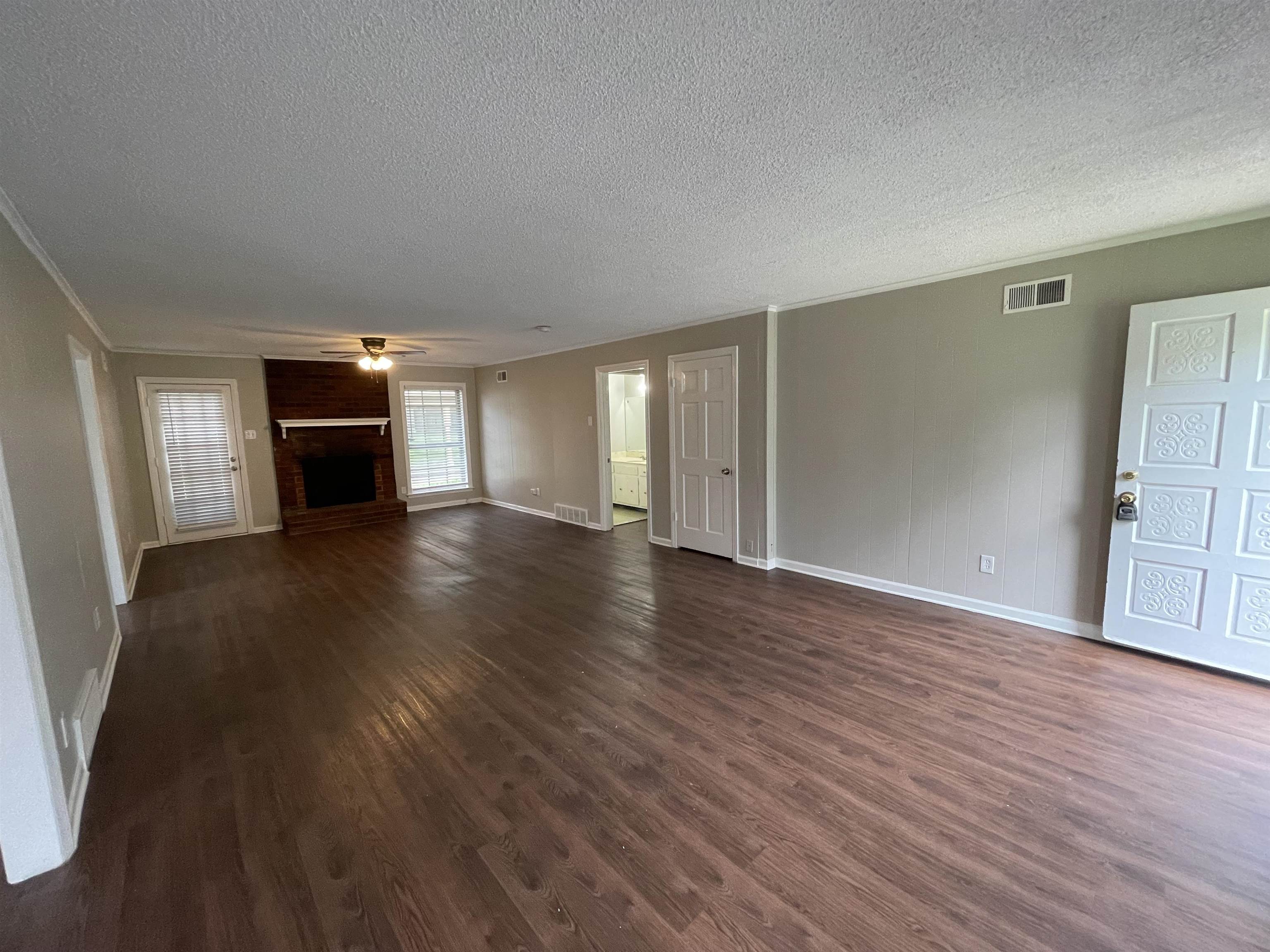 5414 Maple Ridge Road Memphis, TN 38134 - Photo 6 of 23 Unfurnished living room featuring brick wall, a fireplace, a textured ceiling, dark wood-type flooring, and ceiling fan