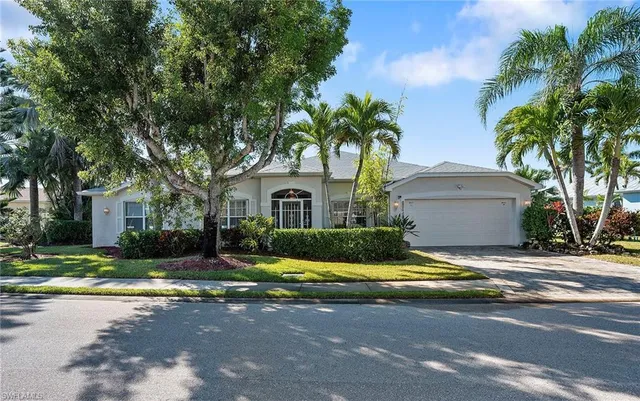 a view of yellow house with a yard and palm trees