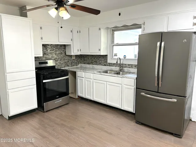 a kitchen with stainless steel appliances granite countertop a refrigerator a sink a stove and white cabinets