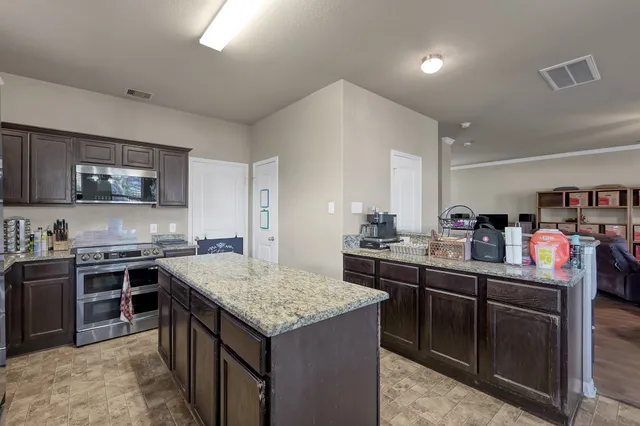 a kitchen with stainless steel appliances granite countertop a stove top oven a sink dishwasher a dining table and chairs with wooden floor