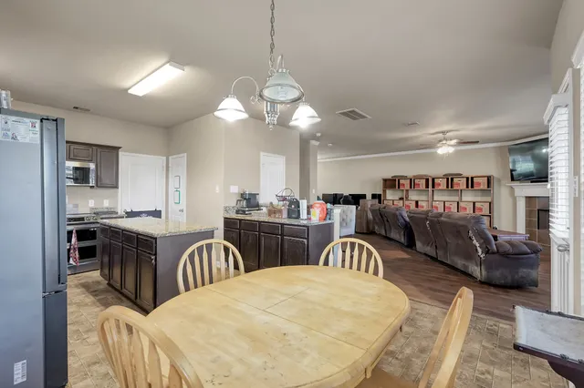 a kitchen with stainless steel appliances granite countertop a stove a refrigerator a oven a dining table and chairs with wooden floor