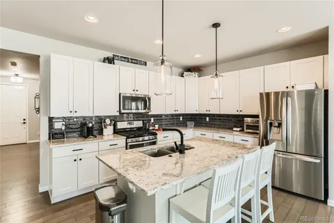 a kitchen with stainless steel appliances granite countertop a refrigerator a sink dishwasher a stove a dining table and chairs with wooden floor