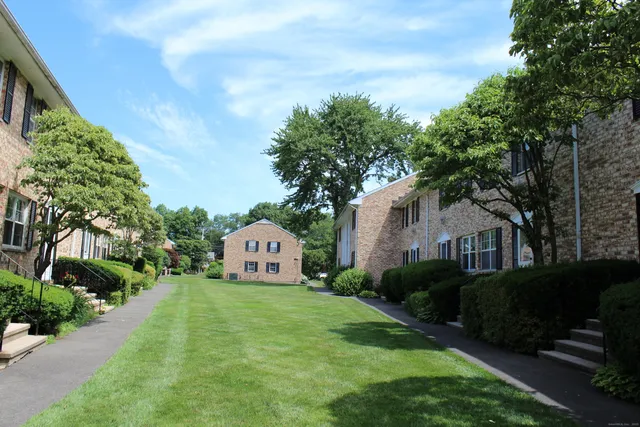 a view of a white house with a big yard plants and large trees