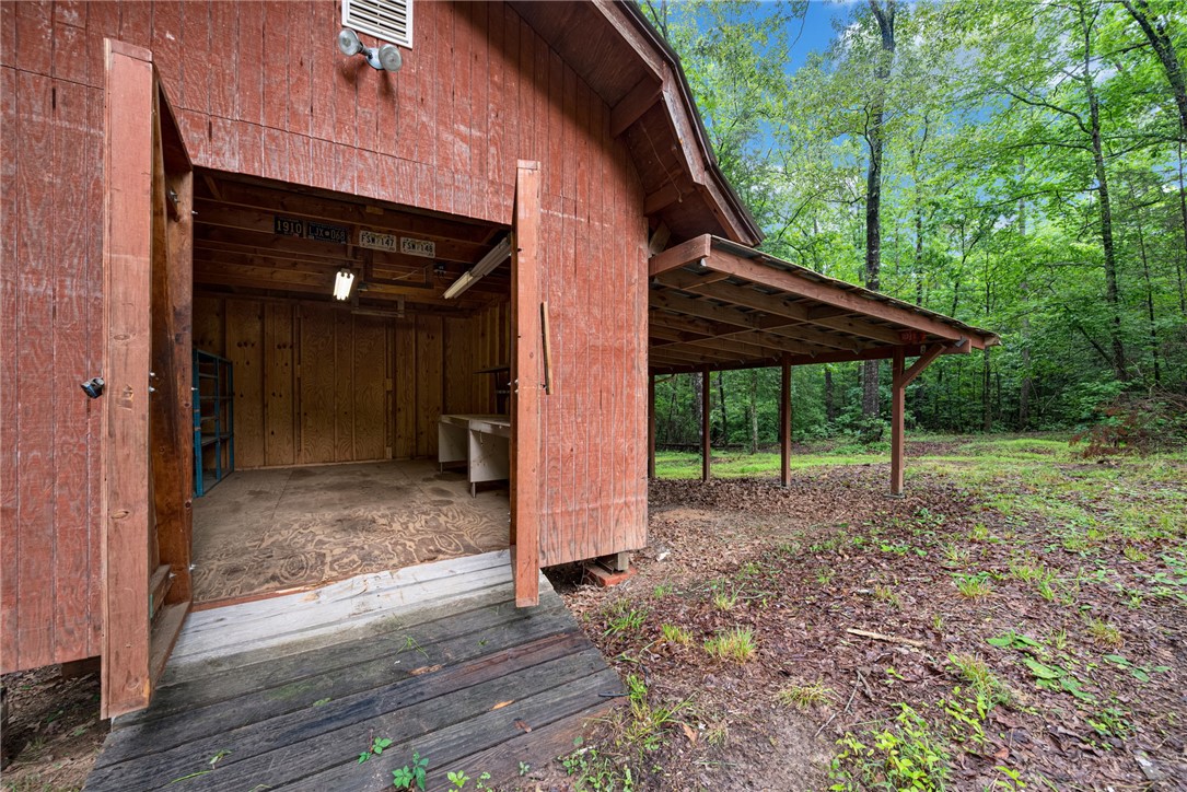 237 Spring Valley Road Liberty, SC 29657 - Photo 28 of 50 A rustic barn with an open lean-to shelter, perfect for equipment storage or a workshop, sits amidst a verdant wooded landscape.