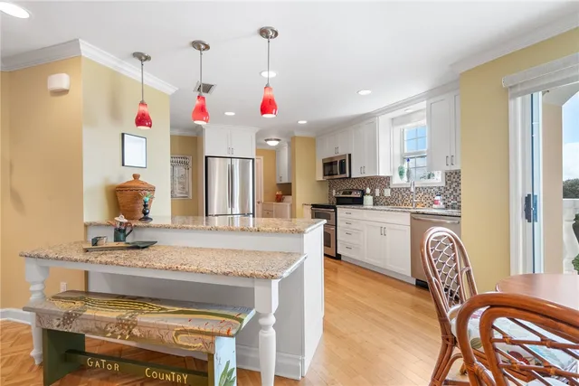 a kitchen with stainless steel appliances granite countertop a sink a stove a refrigerator cabinets and a dining table