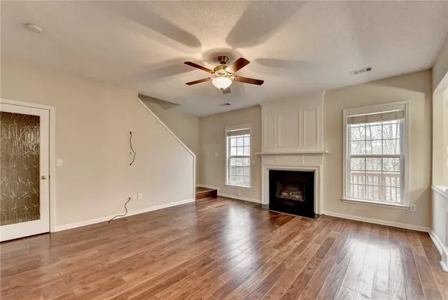 a view of an empty room with wooden floor fireplace and a window