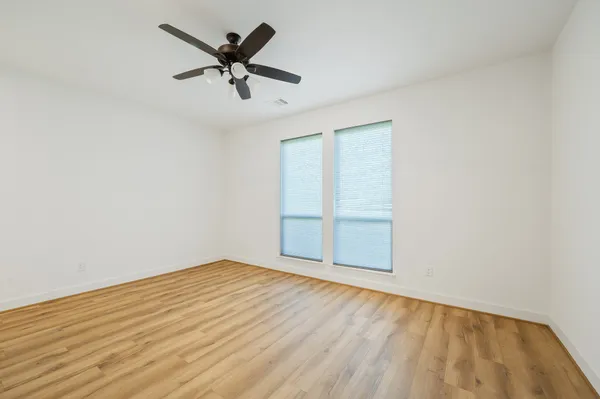an empty room with wooden floor fan and windows