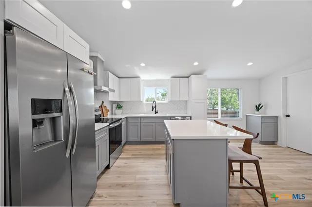 a kitchen with stainless steel appliances kitchen island granite countertop a refrigerator a sink a stove a dining table and chairs