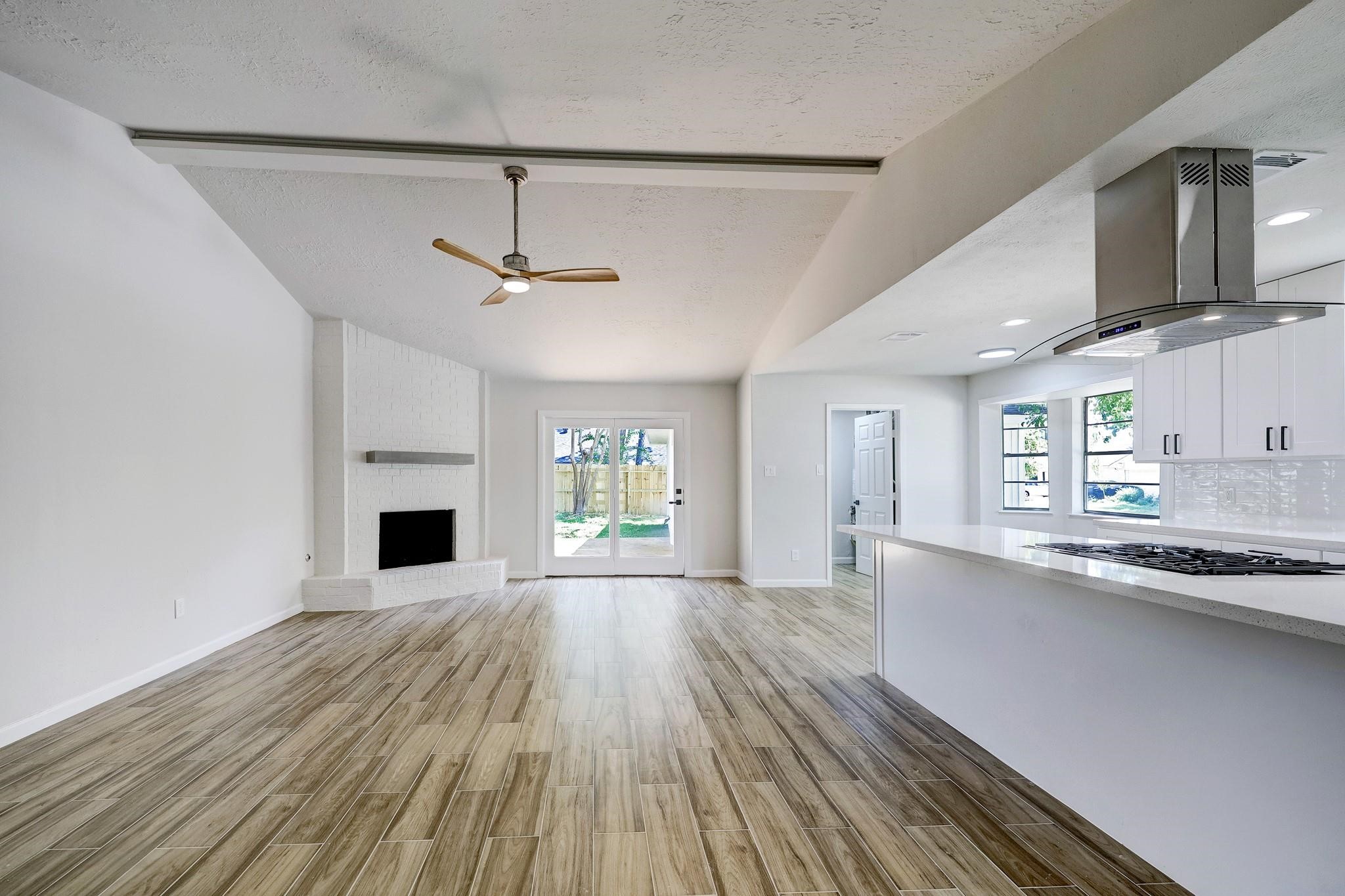 9723 Galston Lane Spring, TX 77379 - Photo 11 of 24 The expansive living room features vaulted ceilings and wood-look flooring. A floor-to-ceiling fireplace with a custom mantle adds warmth and character. The open layout effortlessly connects to the kitchen and breakfast area.