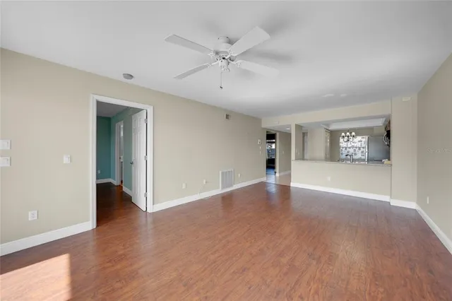 a view of an empty room with wooden floor and a ceiling fan