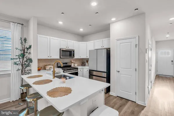 a kitchen with stainless steel appliances granite countertop a refrigerator a stove a sink a oven a dining table and chairs with wooden floor