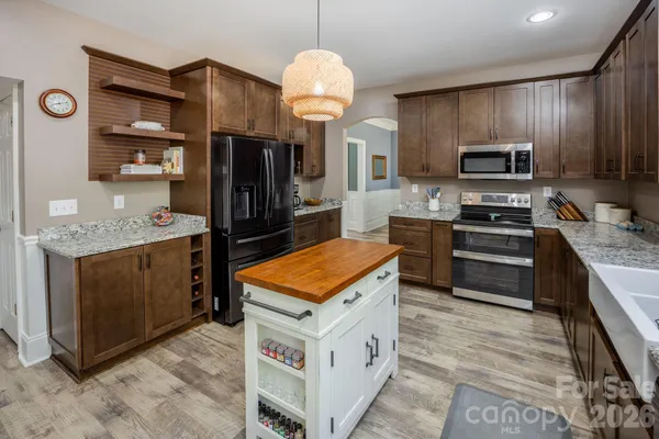 a kitchen with stainless steel appliances granite countertop a stove top oven a sink dishwasher a refrigerator and a dining table with wooden floor