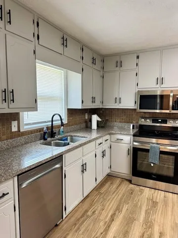 a kitchen with granite countertop a sink stainless steel appliances and white cabinets