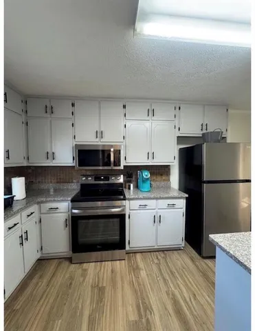 a kitchen with stainless steel appliances granite countertop a stove top oven a refrigerator a sink and dishwasher with wooden floor