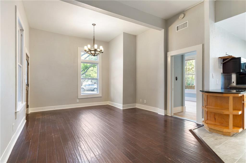 3210 Hampton Road, Unit A B C Austin, TX 78705 - Photo 41 of 42 Hardwood-style flooring throughout a spacious room with a prominent window, white trim, and a classic chandelier