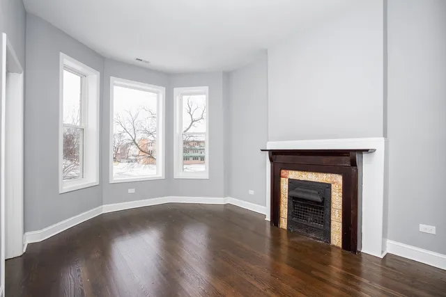 an empty room with wooden floor fireplace and windows