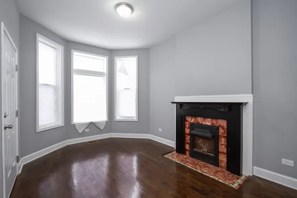 an empty room with wooden floor fireplace and windows