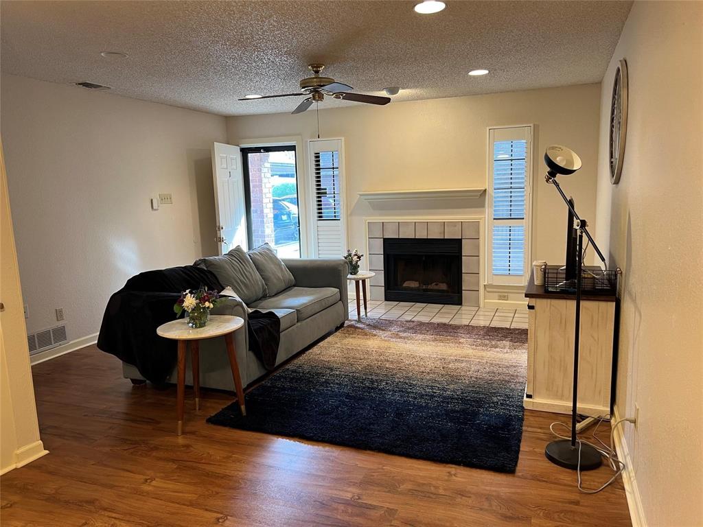 3129 Sappington Place Fort Worth, TX 76116 - Photo 2 of 15 Living room featuring a textured ceiling, a tiled fireplace, dark wood finished floors, and ceiling fan