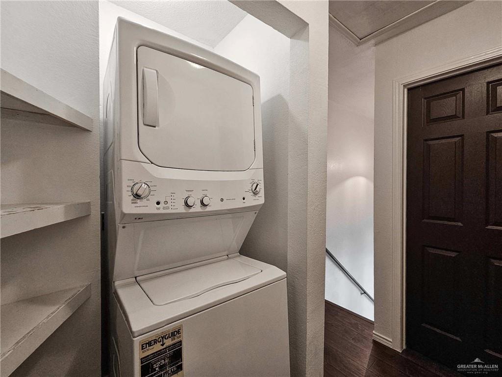 2201 South Jackson Road, Unit 2I Pharr, TX 78577 - Photo 16 of 23 Dedicated laundry area featuring a stacked washer and dryer, adjacent to built-in shelving, a dark wood-paneled door, and wood-finish flooring extending into a hallway