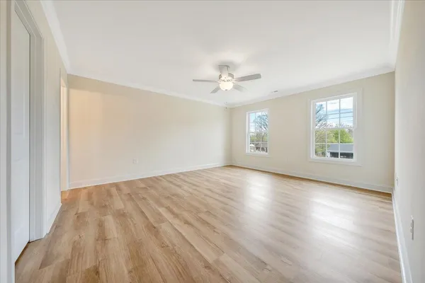 an empty room with wooden floor chandelier fan and windows
