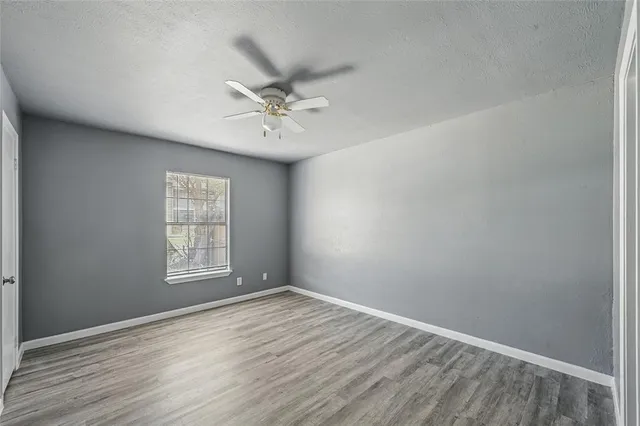 an empty room with wooden floor fan and windows
