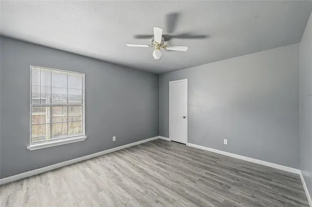 an empty room with wooden floor chandelier fan and windows