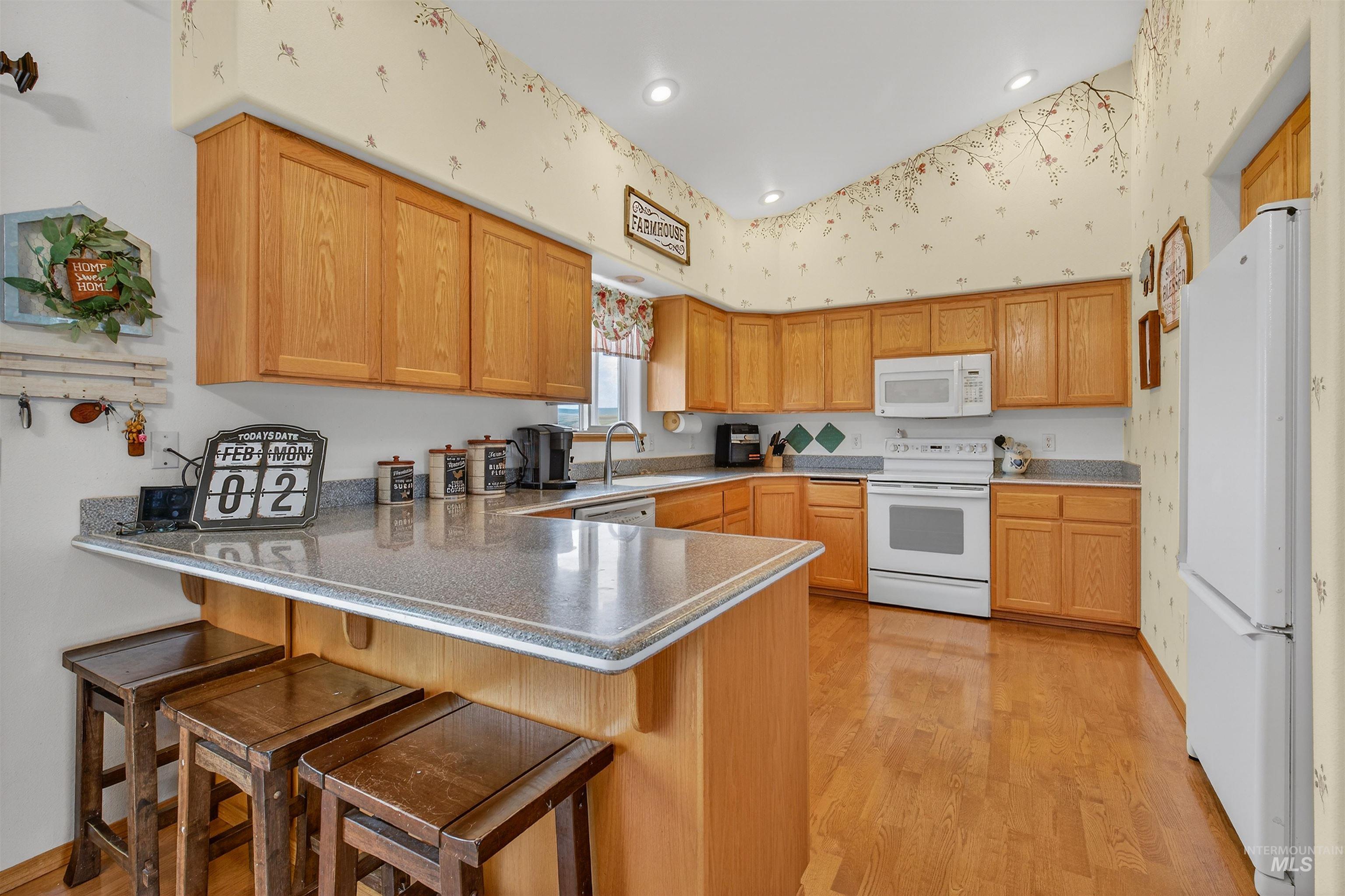 3737 19th Street Lewiston, ID 83501 - Photo 13 of 40 Kitchen with a peninsula, a kitchen bar, white appliances, wallpapered walls, and light wood-type flooring