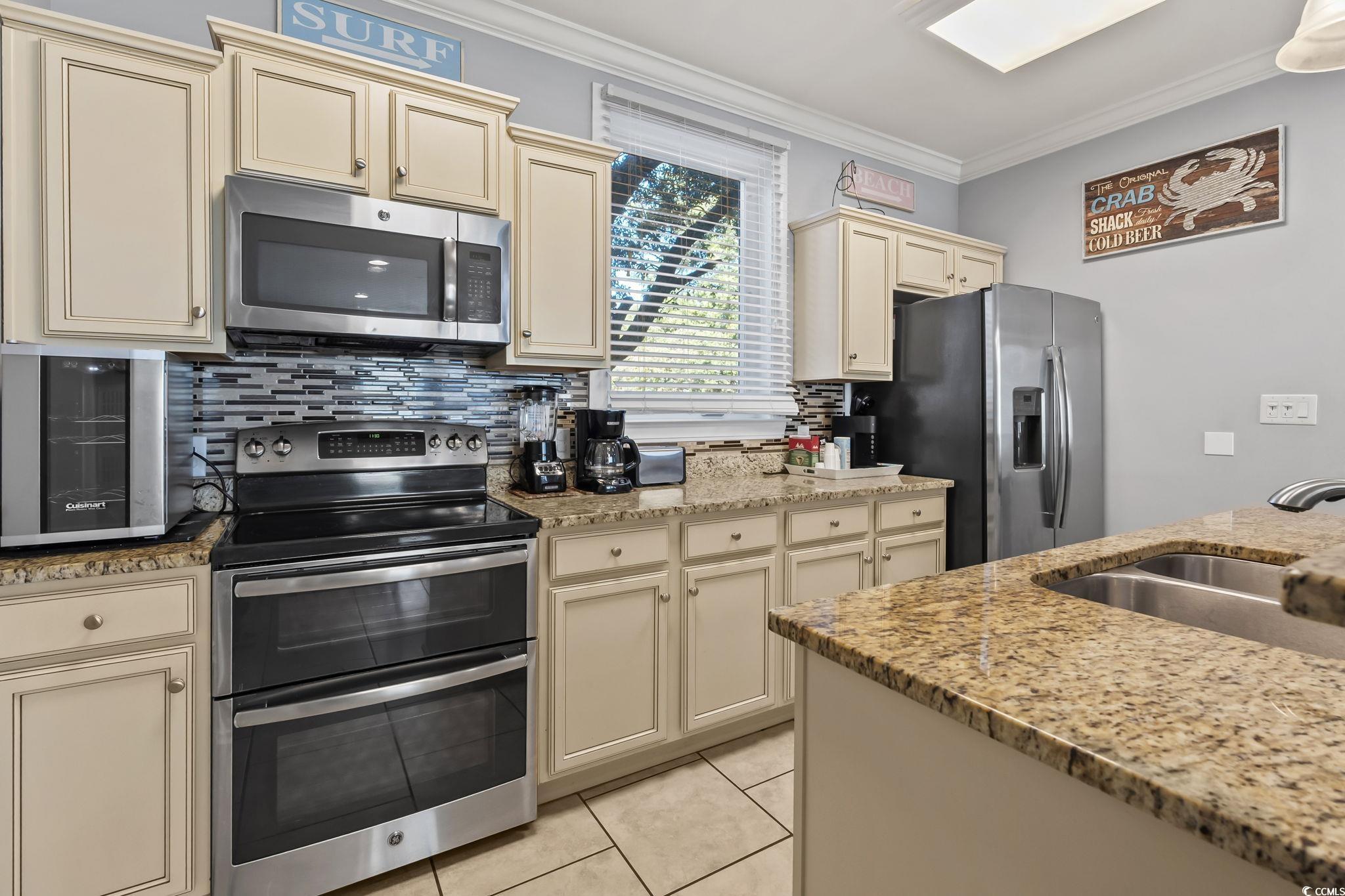 7401 North Ocean Boulevard, Unit 5 Myrtle Beach, SC 29572 - Photo 6 of 34 Kitchen with cream cabinets, appliances with stainless steel finishes, crown molding, light stone countertops, and tasteful backsplash