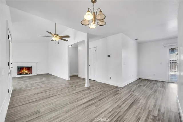 an empty room with wooden floor a chandelier fan and windows