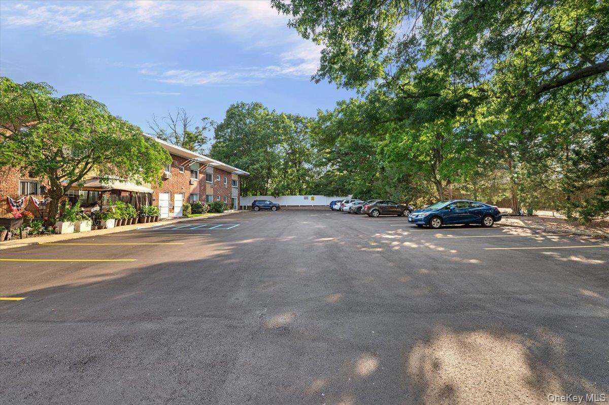 267 North Newbridge Road, Unit 2D Levittown, NY 11756 - Photo 19 of 22 Paved parking area featuring striped parking spaces, a brick-facade building, and mature surrounding trees