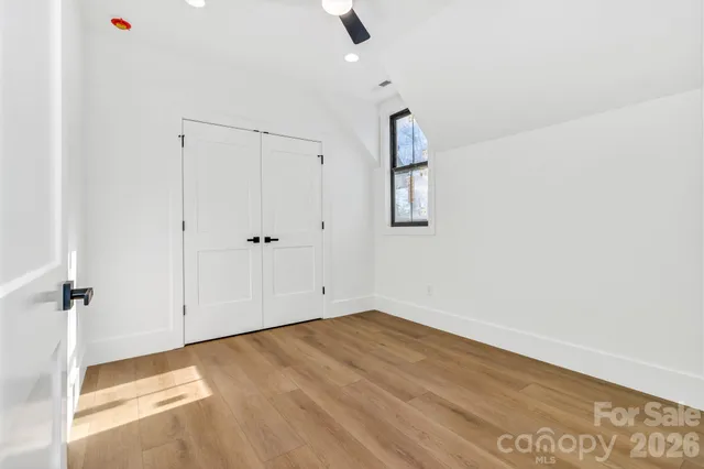 an empty room with wooden floor closet and windows