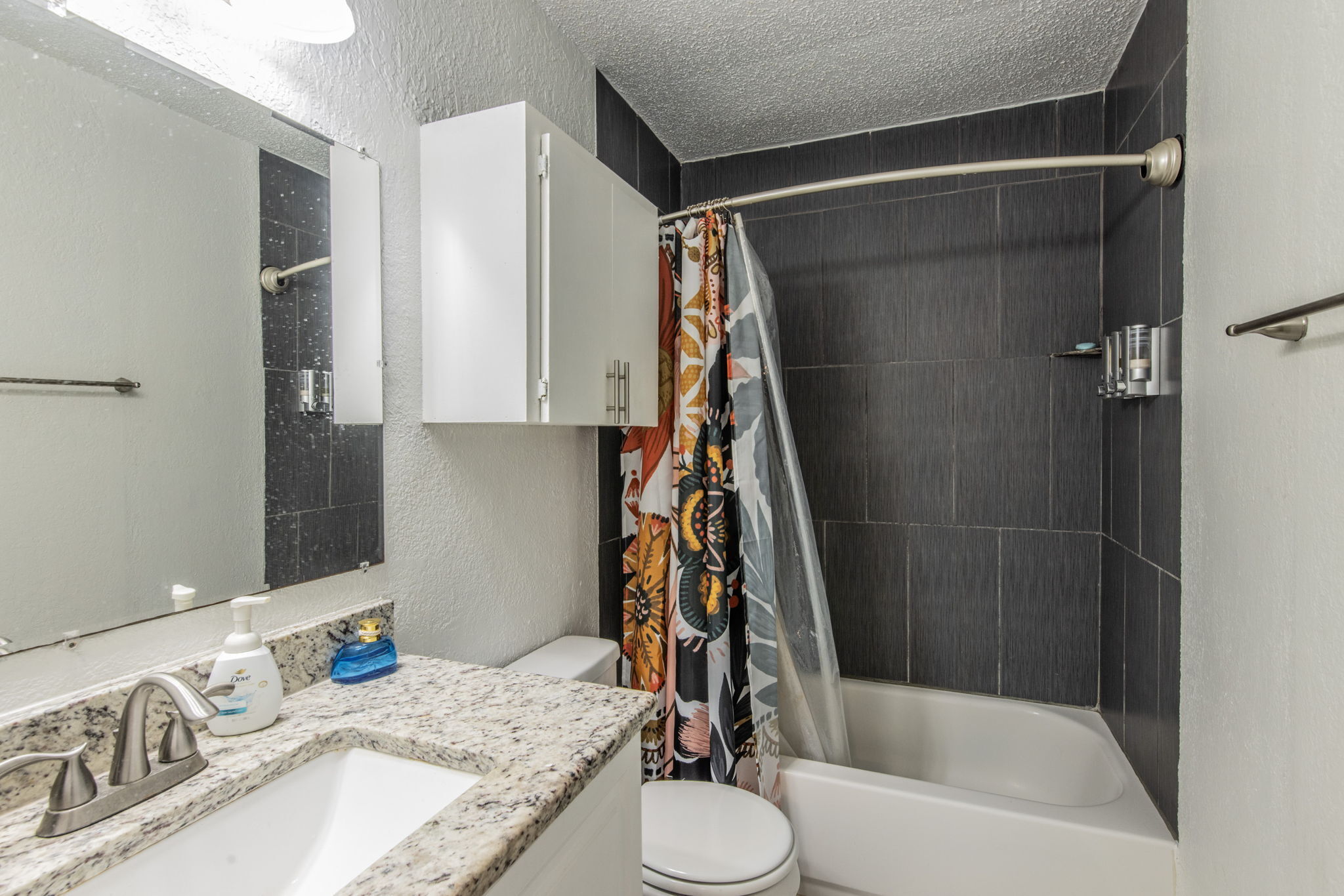 1008 Milford Way Austin, TX 78745 - Photo 33 of 40 Bathroom featuring a shower-tub combination with dark gray tiled surround, a white vanity with a speckled countertop, and a built-in wall cabinet