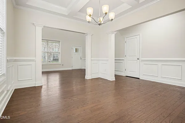 an empty room with wooden floor chandelier and windows