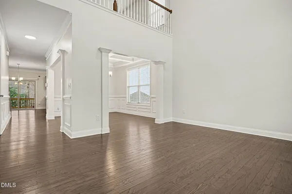 an empty room with wooden floor chandelier and windows