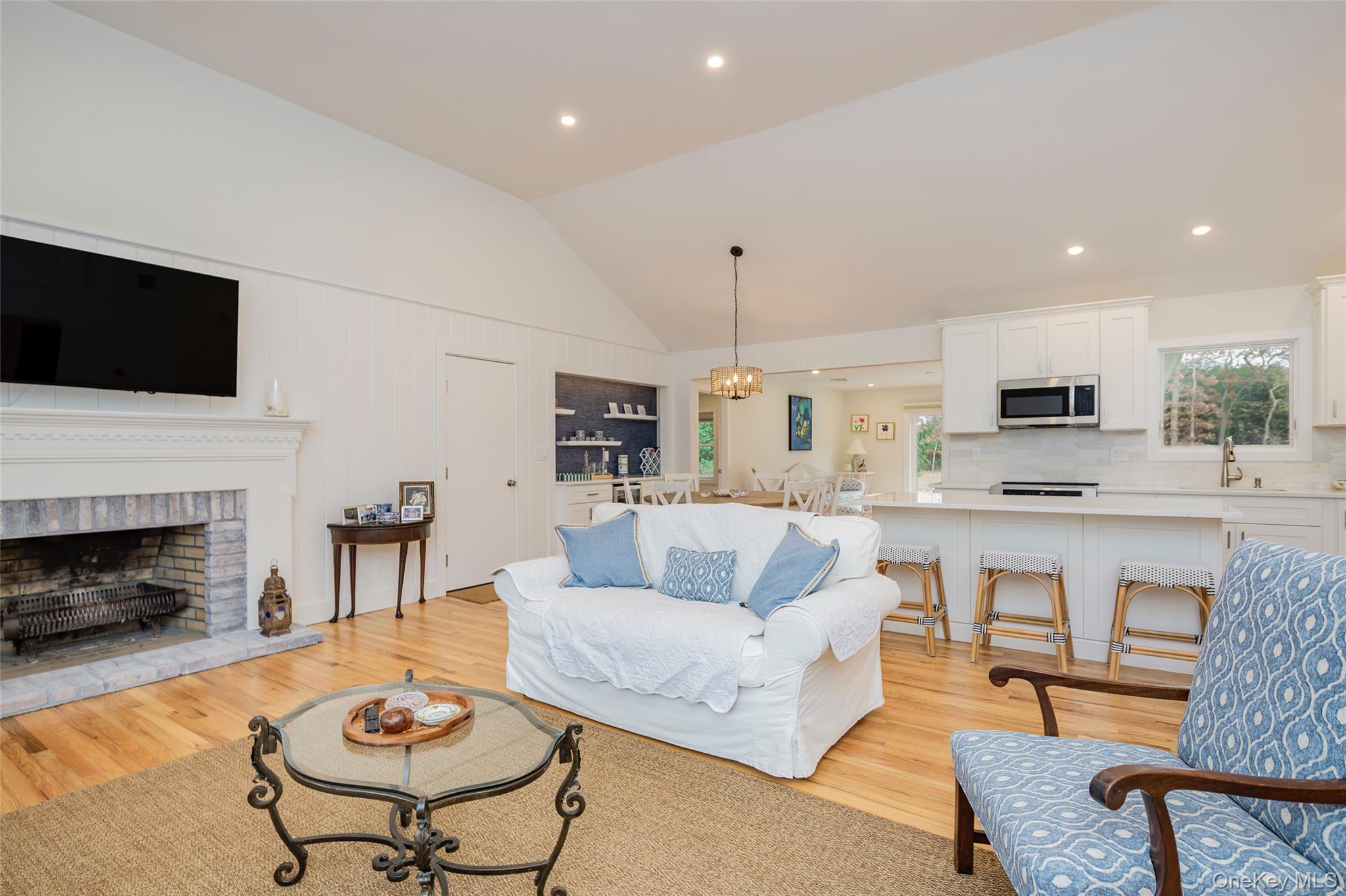 Living room featuring lofted ceiling, a chandelier, light wood-style flooring, recessed lighting, and a brick fireplace