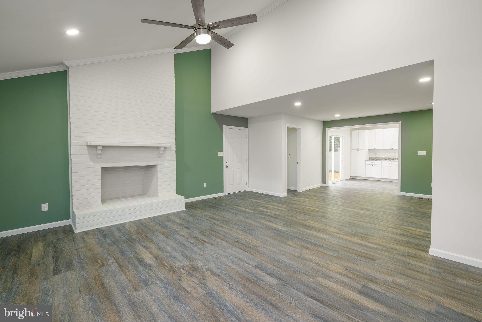 16853 Sherbrooke Road Lewes, DE 19958 - Photo 8 of 32 an empty room with wooden floor a ceiling fan and a kitchen