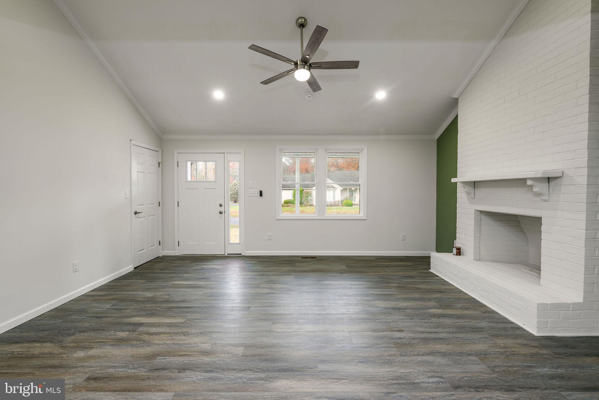16853 Sherbrooke Road Lewes, DE 19958 - Photo 10 of 32 an empty room with wooden floor a ceiling fan a fireplace and windows